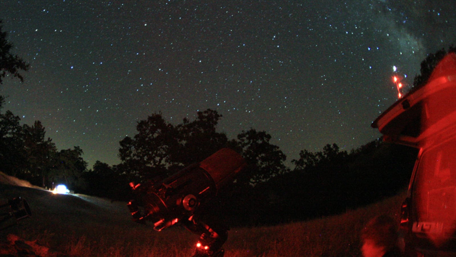 A telescope silhouetted against a starry night sky with the Milky Way arching overhead